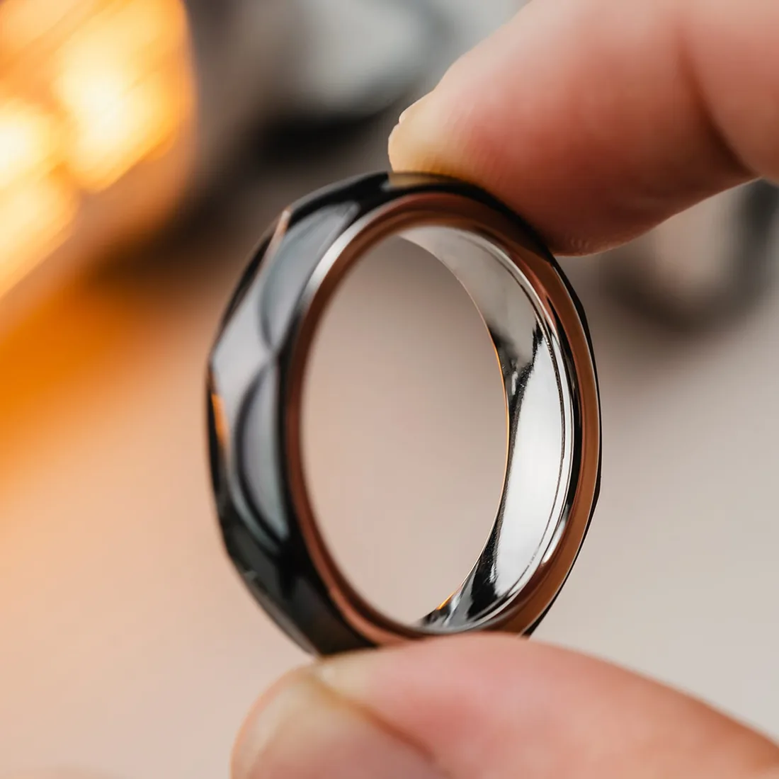 A faceted 01EDC Star Ring held between finger and thumb, warm bokeh behind